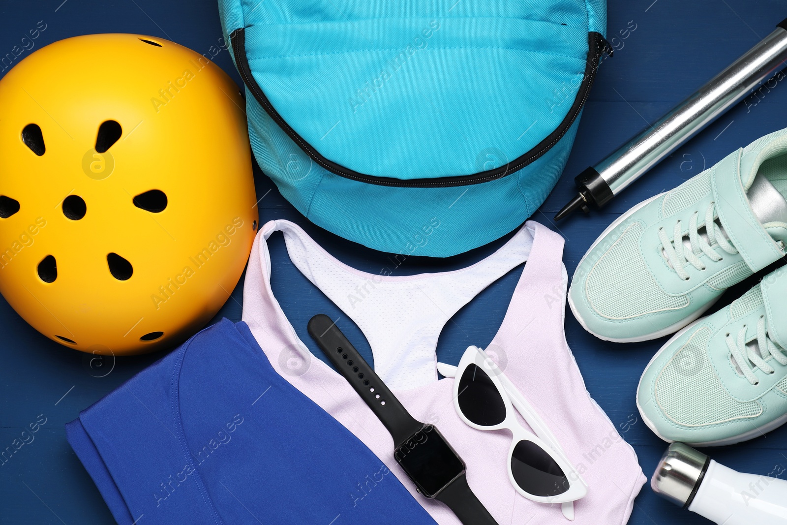 Photo of Bicycle helmet, sneakers, sportswear and accessories on blue wooden background, flat lay