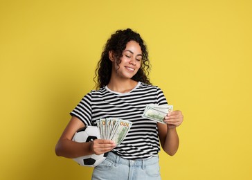 Happy woman with money and soccer ball on yellow background