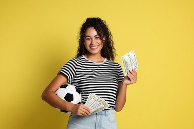 Happy woman with money and soccer ball on yellow background