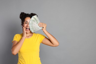 Happy woman with dollar banknotes on grey background, space for text