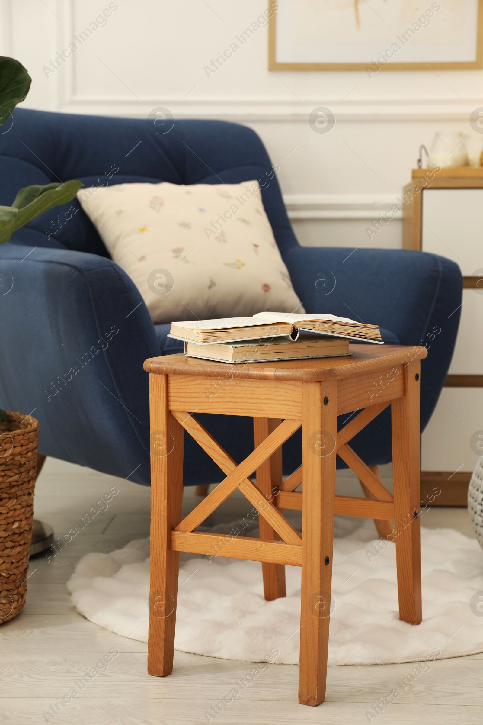 Photo of Stool, books, armchair and houseplant in room. Interior design