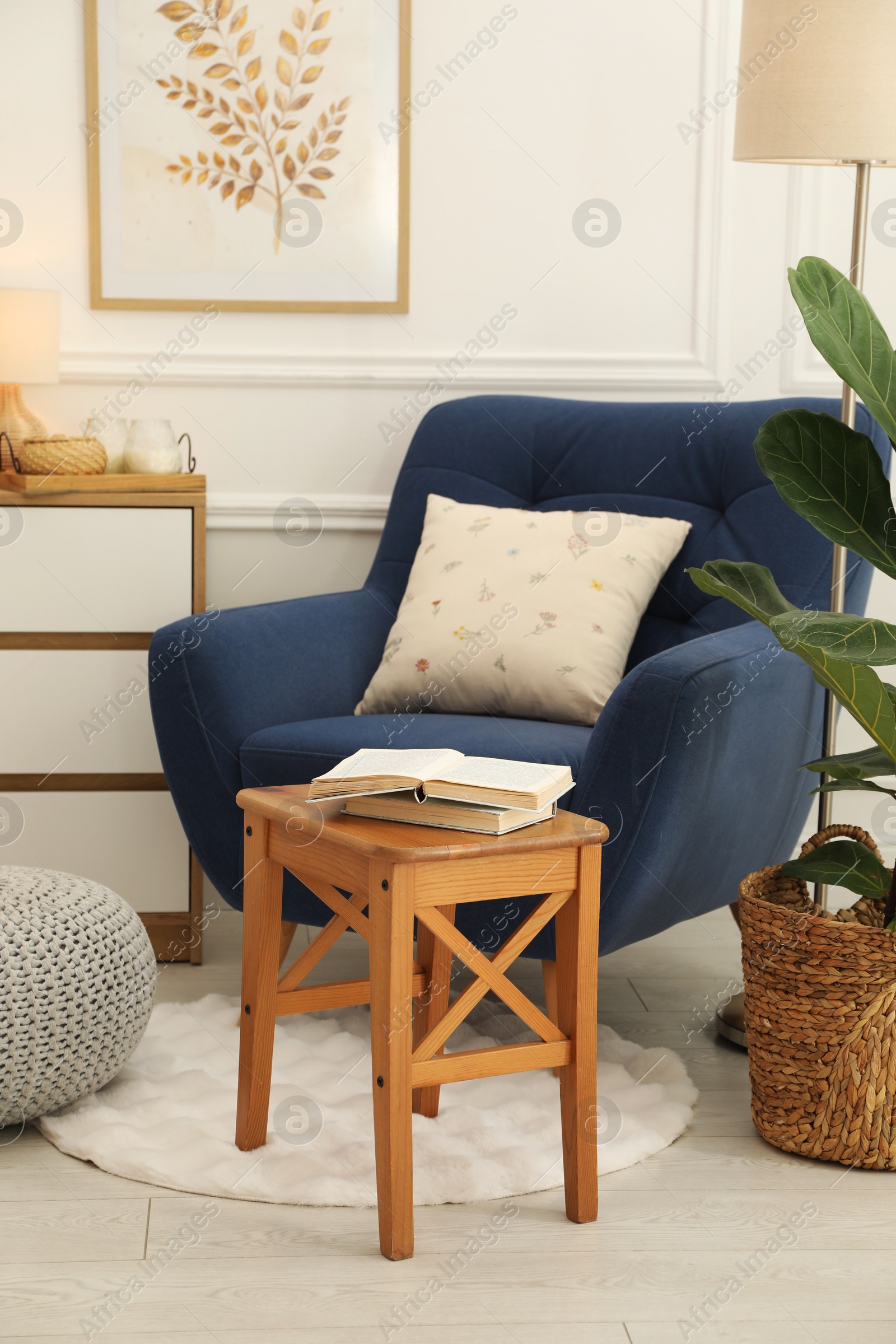 Photo of Stool, books, armchair and houseplant in room. Interior design