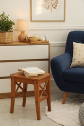 Photo of Stool, books, armchair and houseplant in room. Interior design