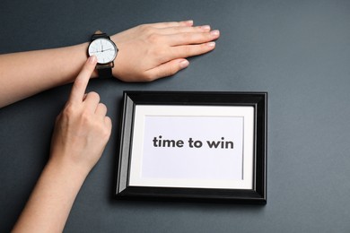 Photo of Woman pointing at watch and frame with words Time To Win on grey background, top view