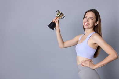 Photo of Happy winner with gold trophy cup on gray background, space for text