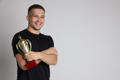 Happy winner with golden trophy cup on light grey background, space for text