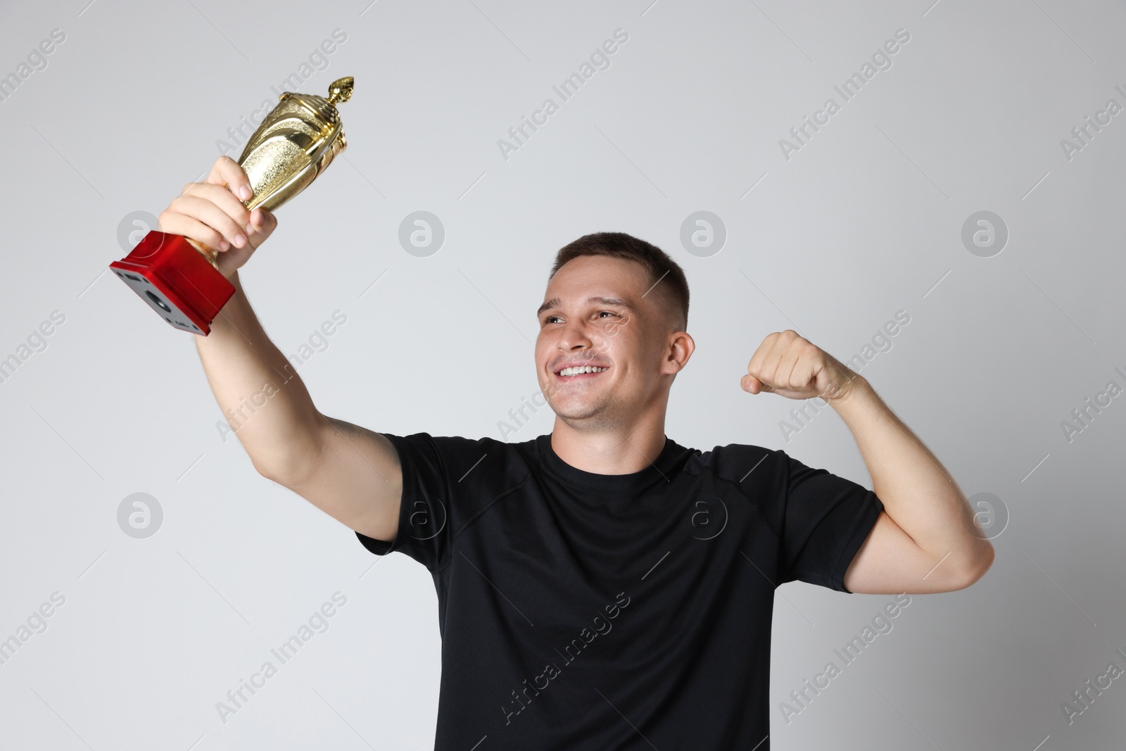 Photo of Happy winner with golden trophy cup on light grey background