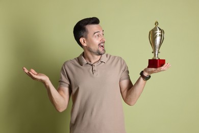 Photo of Happy winner with golden trophy cup on pale olive background