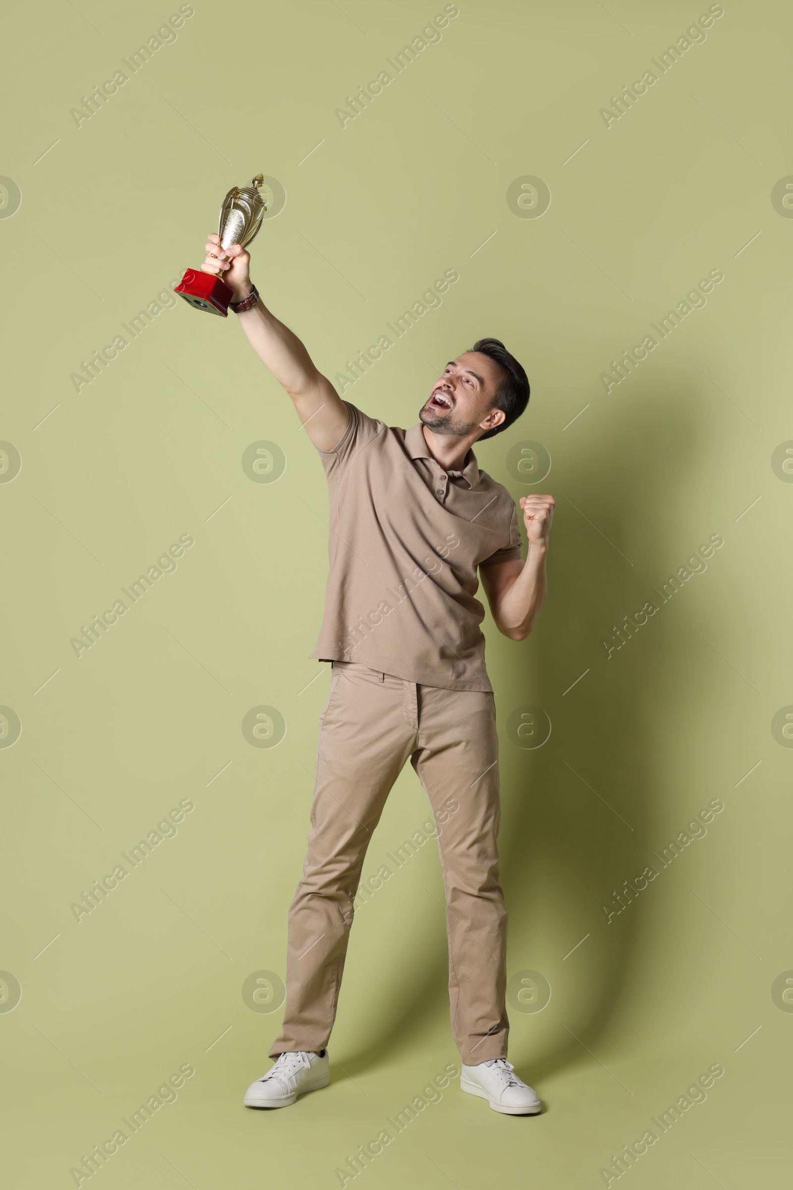 Photo of Happy winner with golden trophy cup on pale olive background