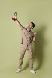 Photo of Happy winner with golden trophy cup on pale olive background