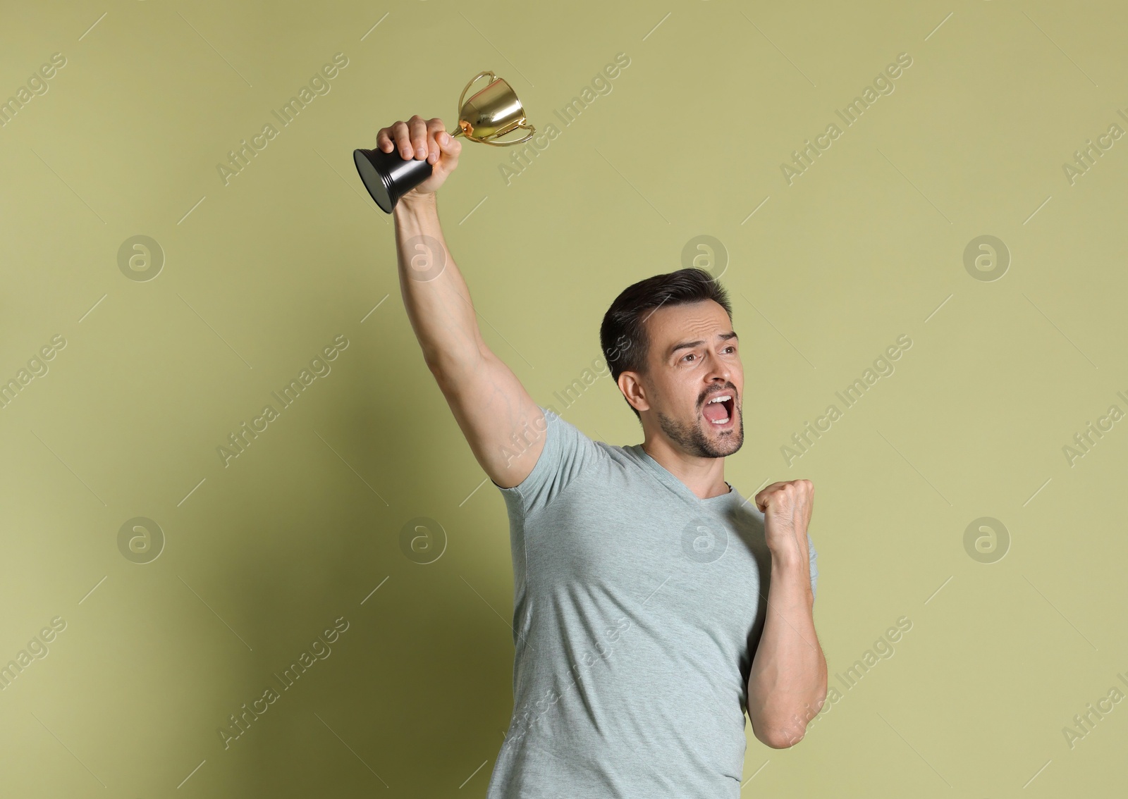 Photo of Emotional winner with golden trophy cup on pale olive background