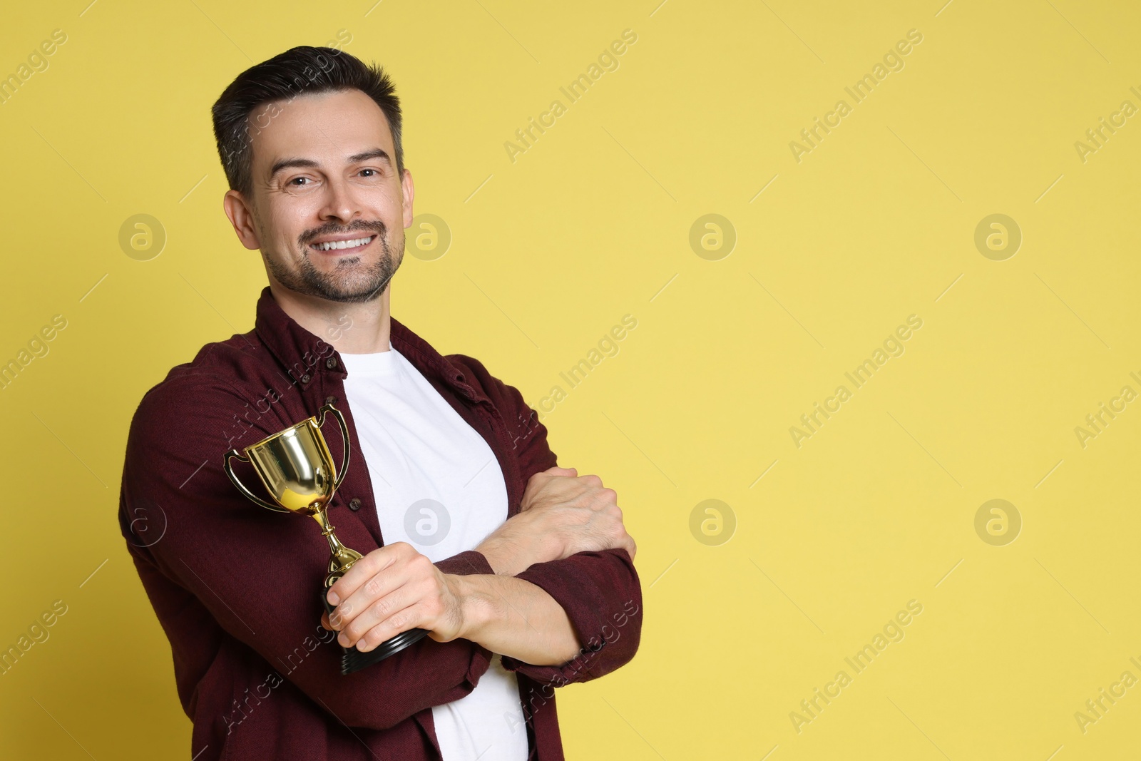 Photo of Happy winner with golden trophy cup on yellow background, space for text