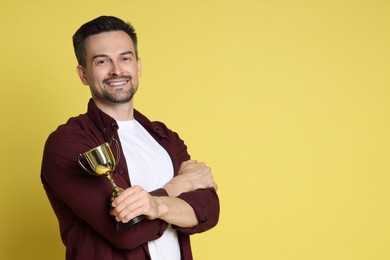 Happy winner with golden trophy cup on yellow background, space for text