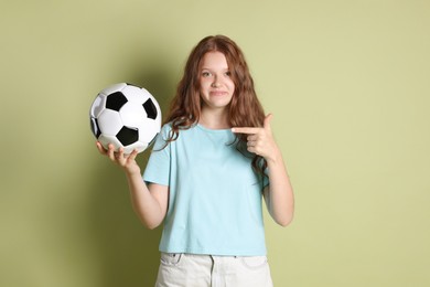 Cute teenage girl pointing at soccer ball on green background