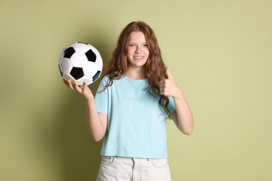 Photo of Smiling teenage girl with soccer ball showing thumbs up on green background