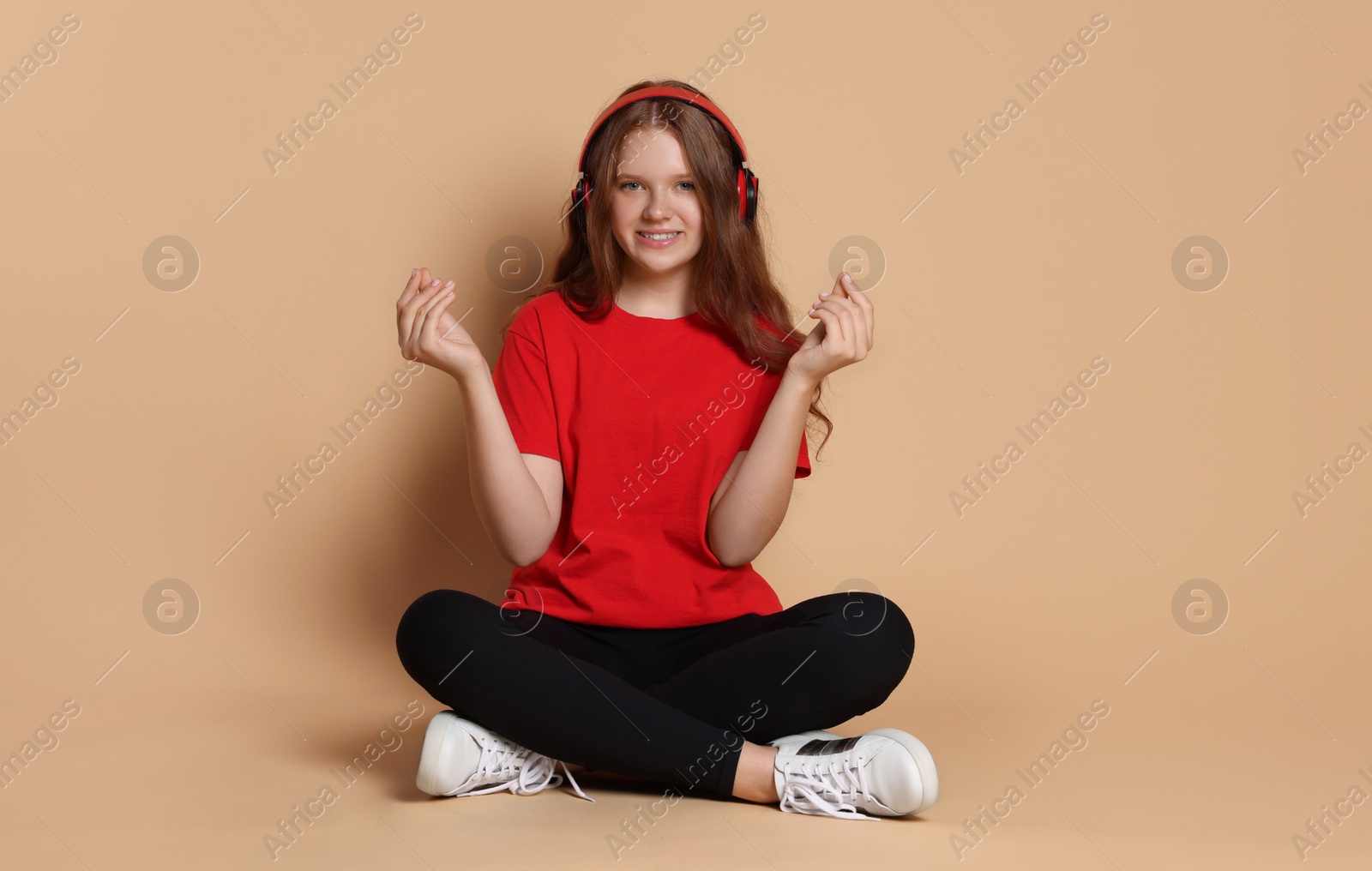 Photo of Smiling teenage girl in headphones listening to music on beige background