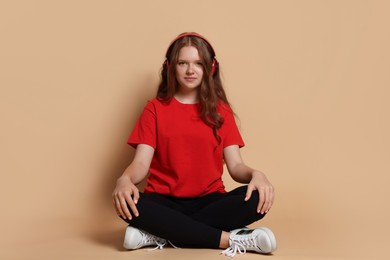 Cute teenage girl in headphones listening to music on beige background