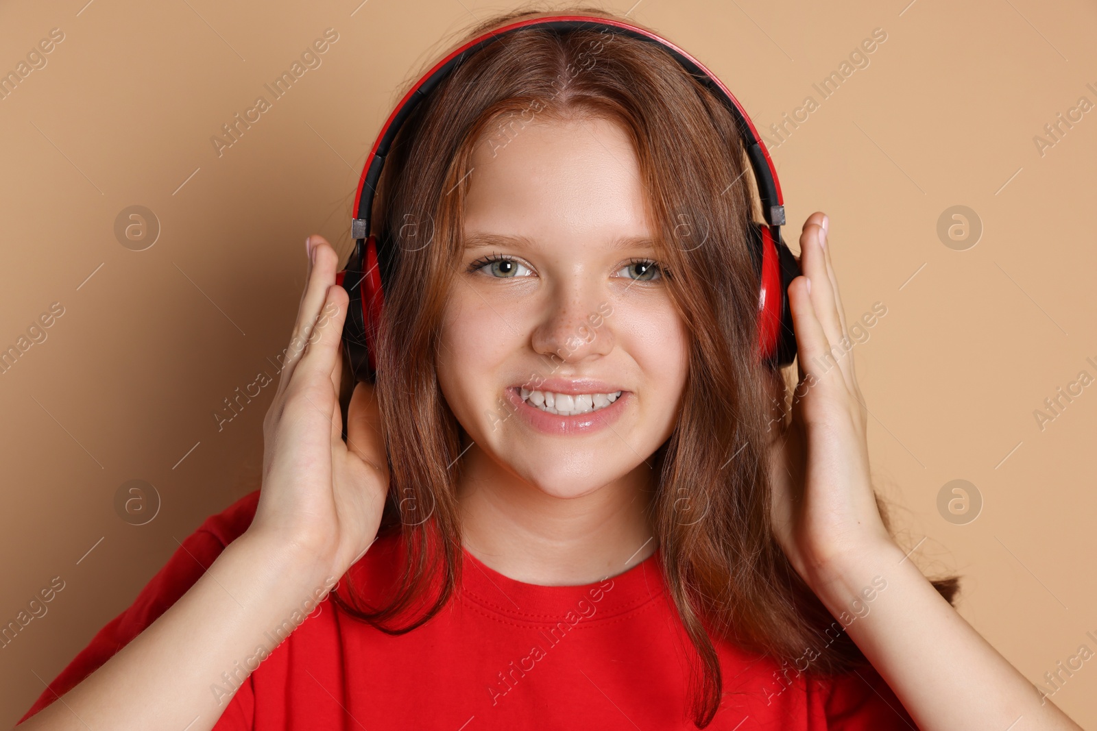 Photo of Smiling teenage girl in headphones listening to music on beige background