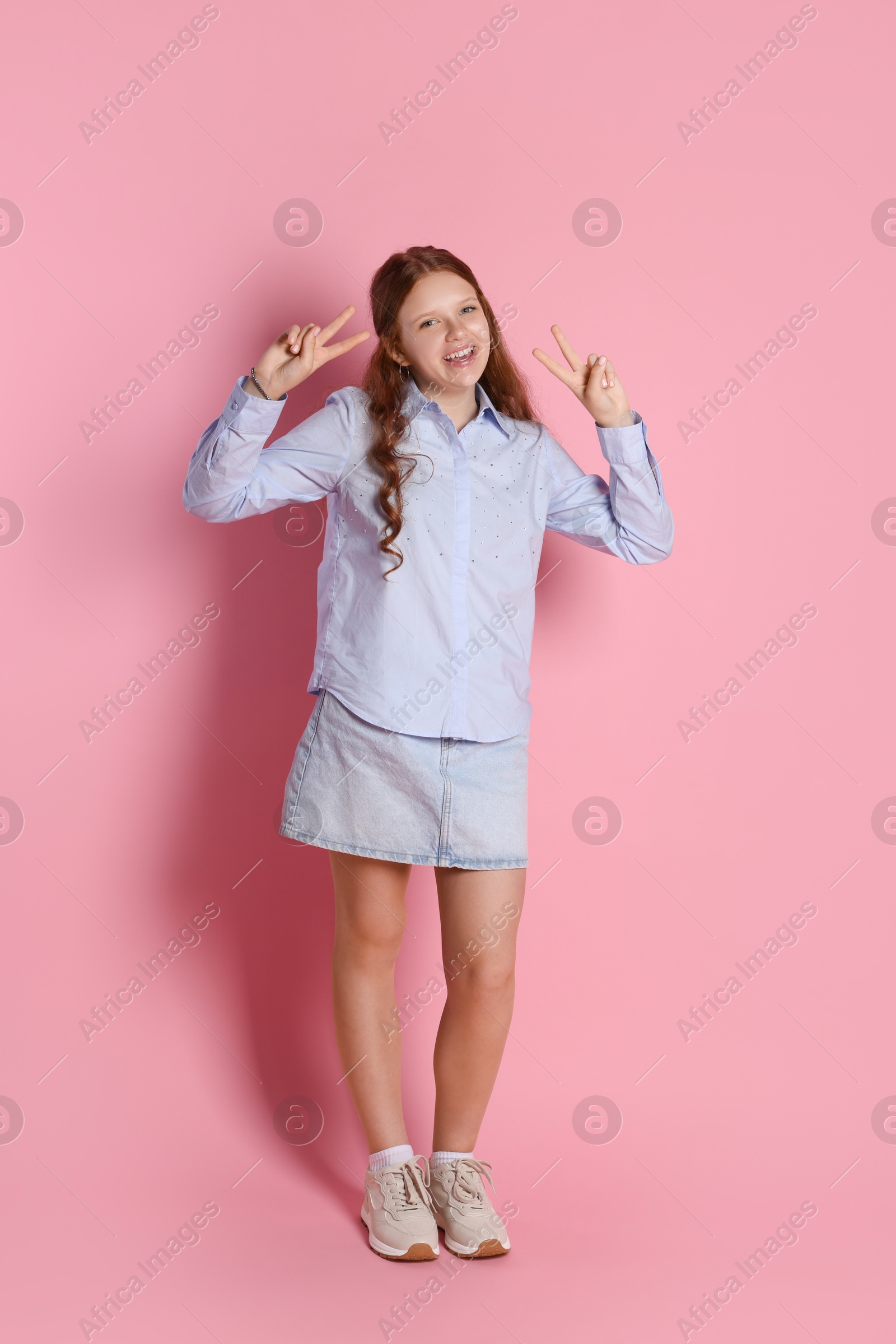 Photo of Happy teenage girl showing peace signs on pink background