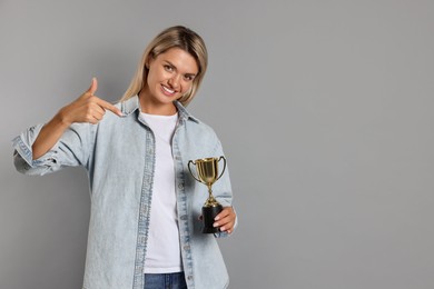 Photo of Happy winner with golden trophy cup on gray background, space for text