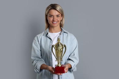 Photo of Happy winner with golden trophy cup on gray background