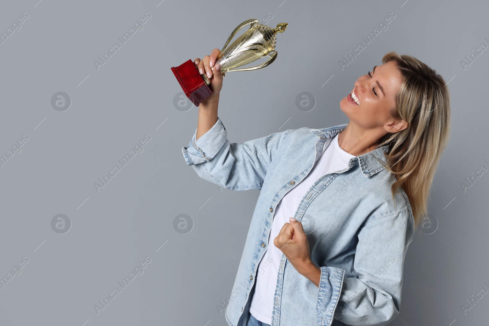 Photo of Happy winner with golden trophy cup on gray background, space for text