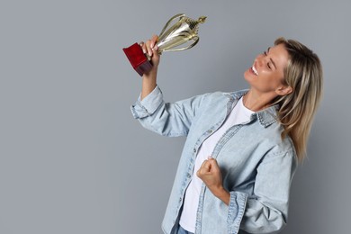 Photo of Happy winner with golden trophy cup on gray background, space for text