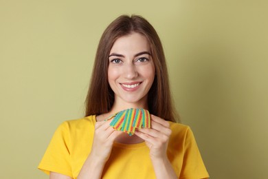 Happy young woman with tasty rainbow sour belts on olive background