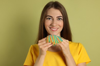 Happy young woman with tasty rainbow sour belts on olive background