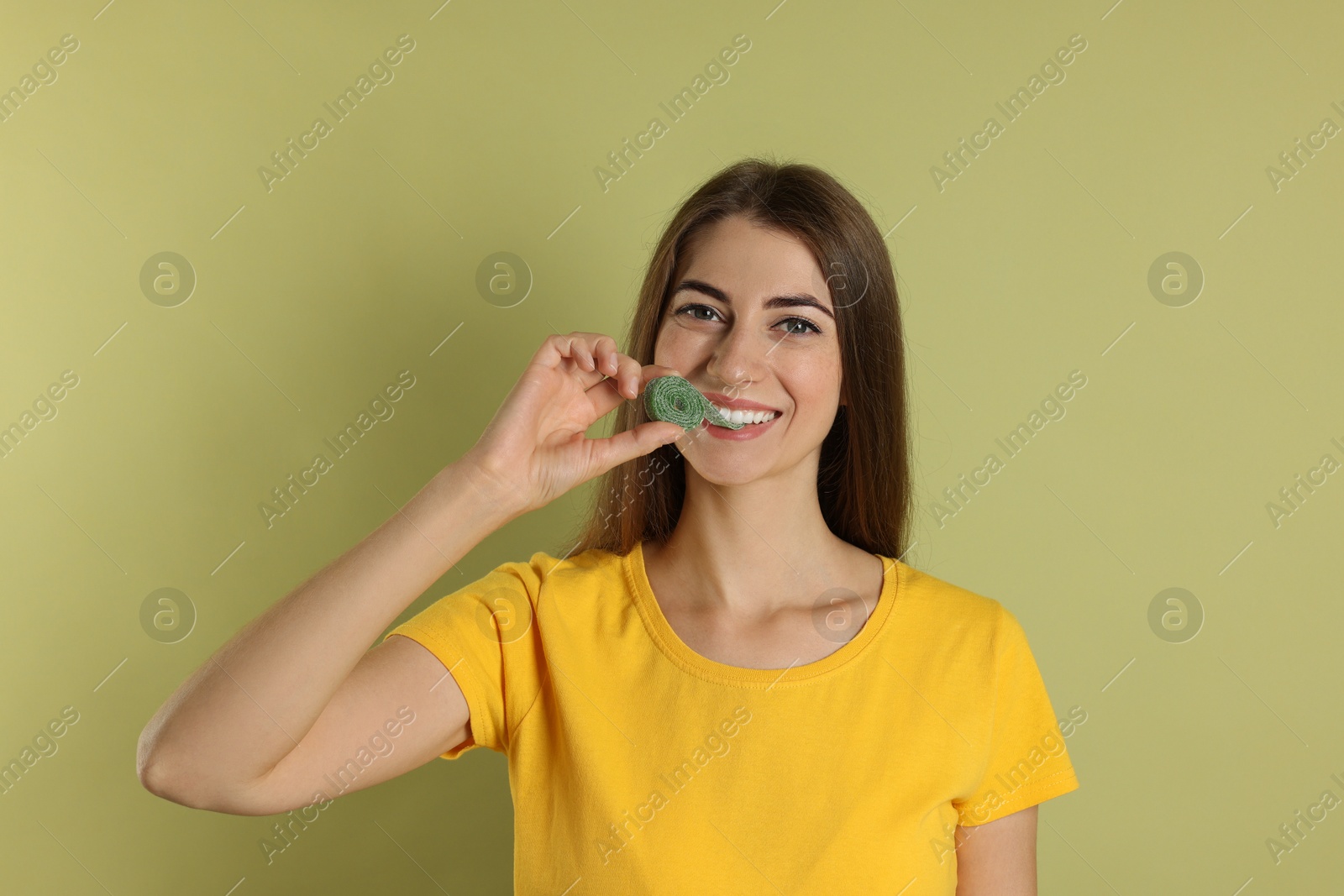 Photo of Young woman eating tasty gummy candy on olive background