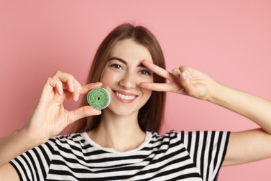 Photo of Happy young woman with tasty gummy candy showing v-sign on pink background