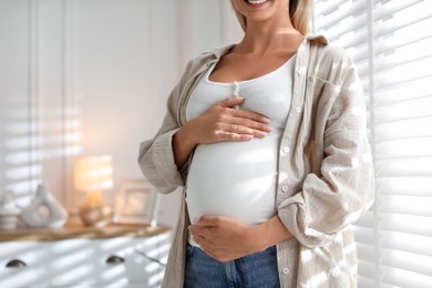 Pregnant woman near window at home, closeup. Space for text