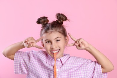 Photo of Happy girl eating tasty gummy candy and showing peace signs on pink background