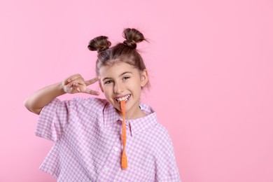 Photo of Happy girl eating tasty gummy candy and showing peace sign on pink background. Space for text