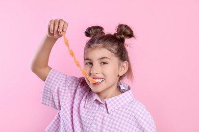 Happy girl eating tasty gummy candy on pink background