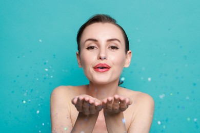 Photo of Woman with perfect makeup blowing confetti on light blue background