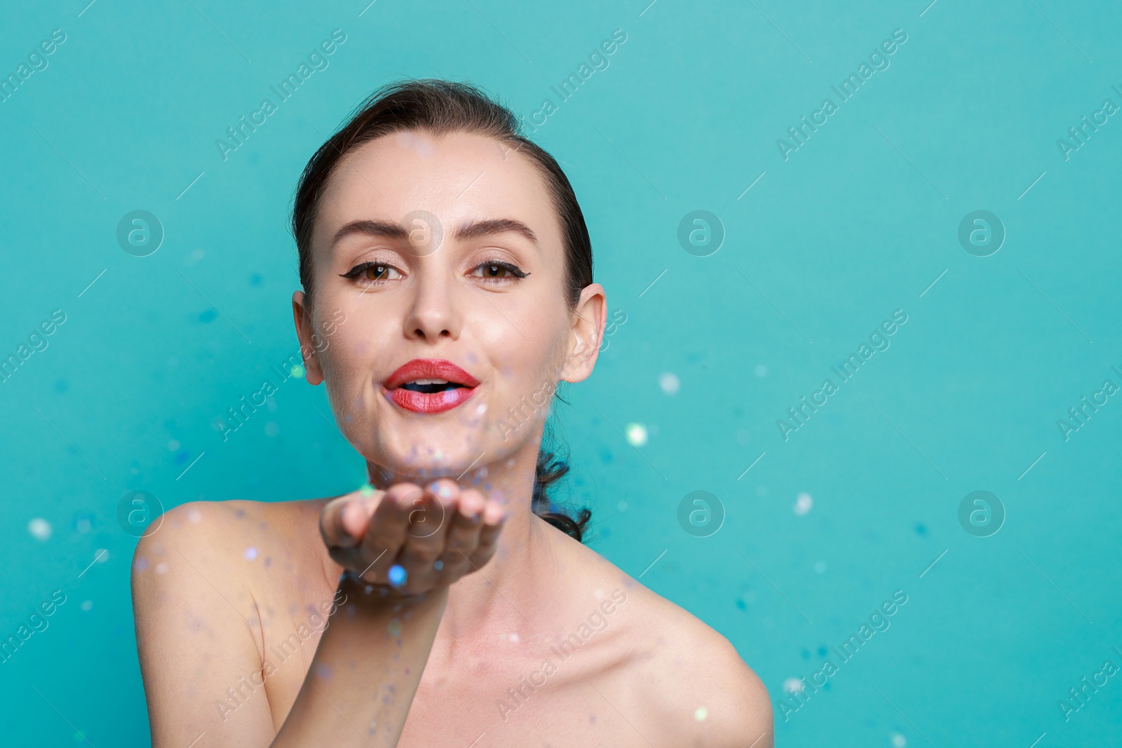 Photo of Woman with perfect makeup blowing confetti on light blue background, space for text