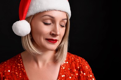 Woman with perfect makeup in Santa hat celebrating Christmas on black background