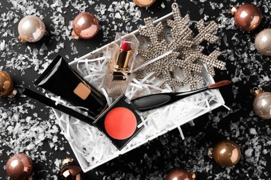 Christmas gift box with decorative cosmetics and festive decor on black background, flat lay