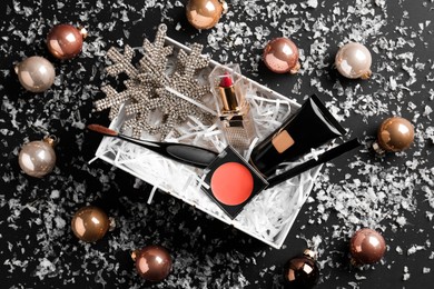 Christmas gift box with decorative cosmetics and festive decor on black background, flat lay