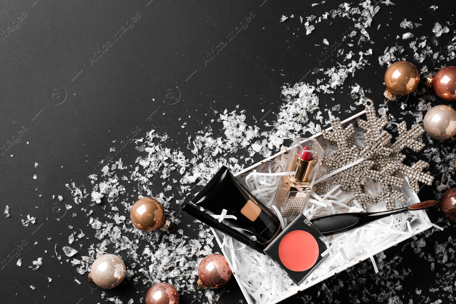 Photo of Christmas gift box with decorative cosmetics and festive decor on black background, flat lay. Space for text