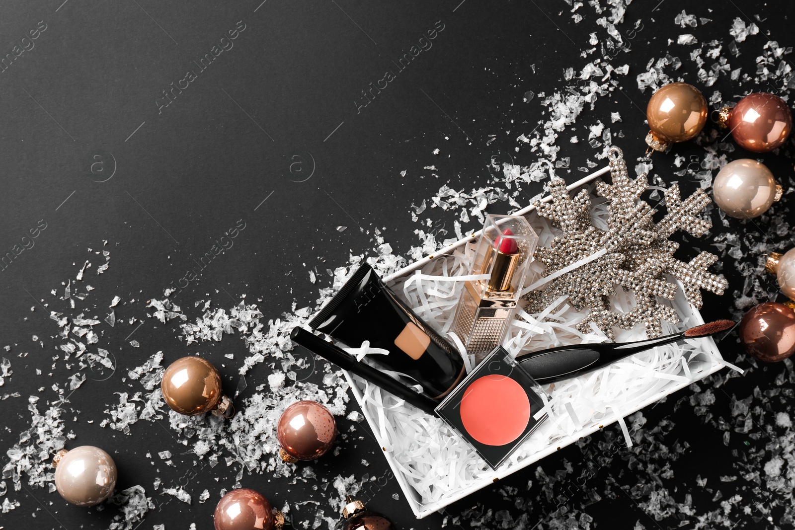 Photo of Christmas gift box with decorative cosmetics and festive decor on black background, flat lay. Space for text