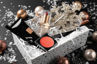 Christmas gift box with decorative cosmetics and festive decor on black background, closeup