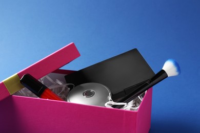 Photo of Gift box with decorative cosmetics on blue background, closeup