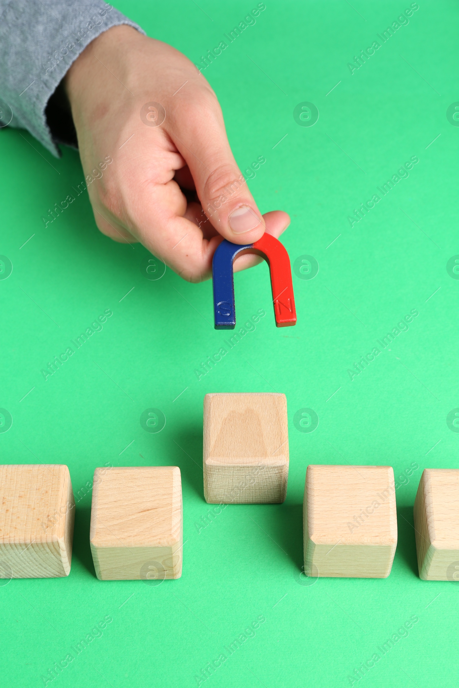 Photo of Man with magnet attracting wooden cubes at green table, closeup