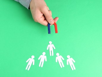 Photo of Man with magnet attracting paper human figures at green table, above view