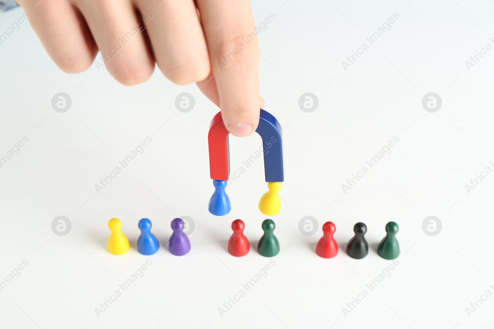 Photo of Man with magnet attracting game pieces at white table, closeup