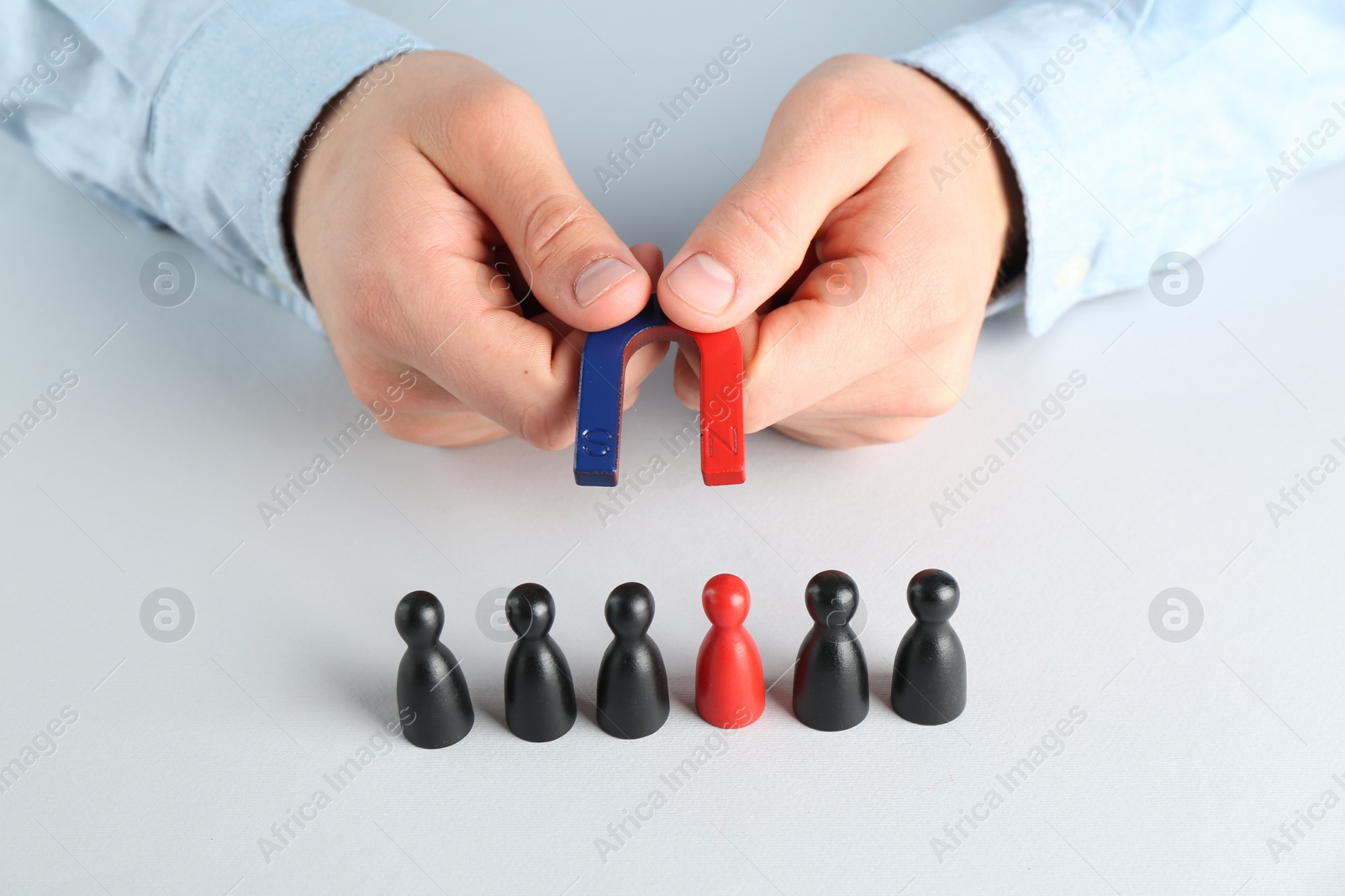 Photo of Man with magnet attracting game pieces at white table, closeup