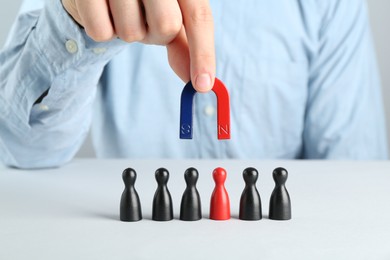 Photo of Man with magnet attracting game pieces at white table, closeup