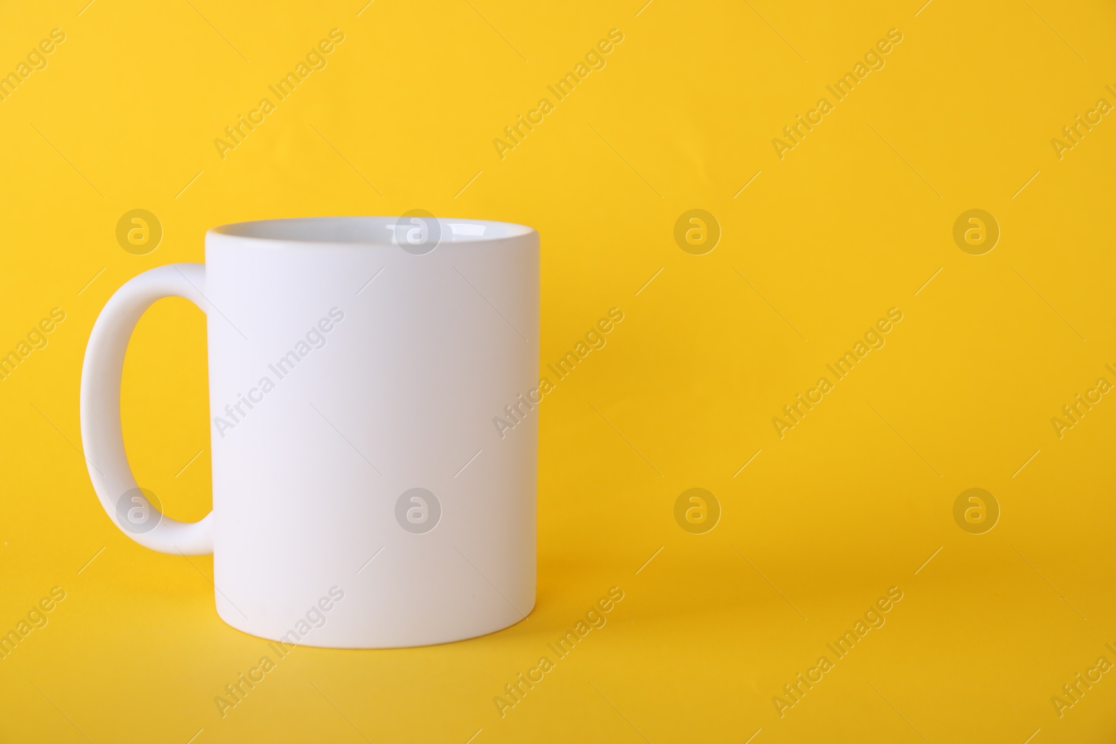 Photo of One blank white mug on yellow background. Mockup for design